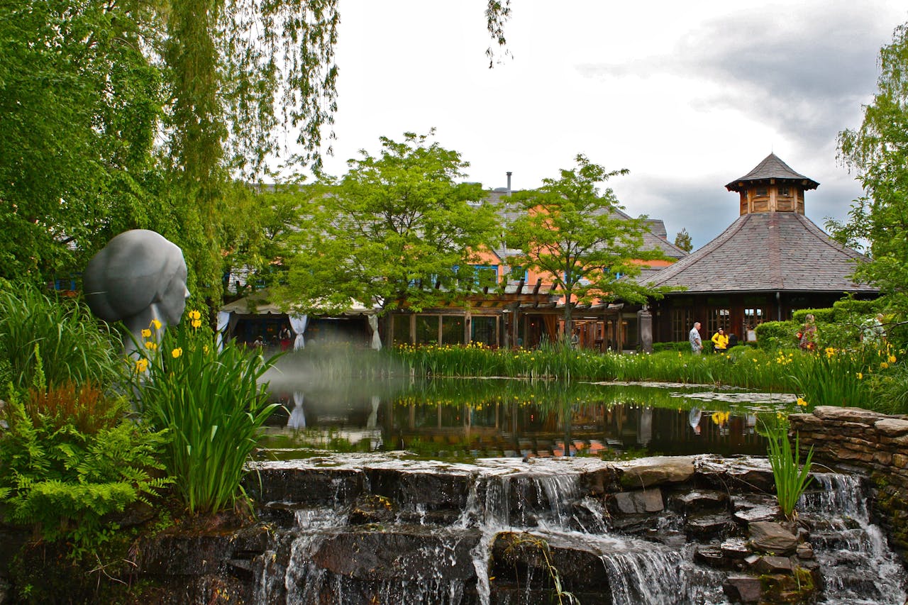 Scenic garden with a pond, waterfall, and sculpture under a cloudy sky.