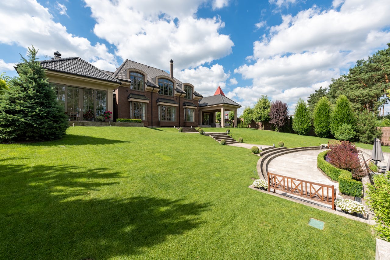 Elegant brick mansion with manicured lawn and garden under a bright blue sky.